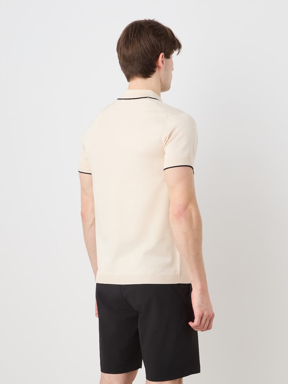 Person wearing a beige polo shirt and black shorts on a light background