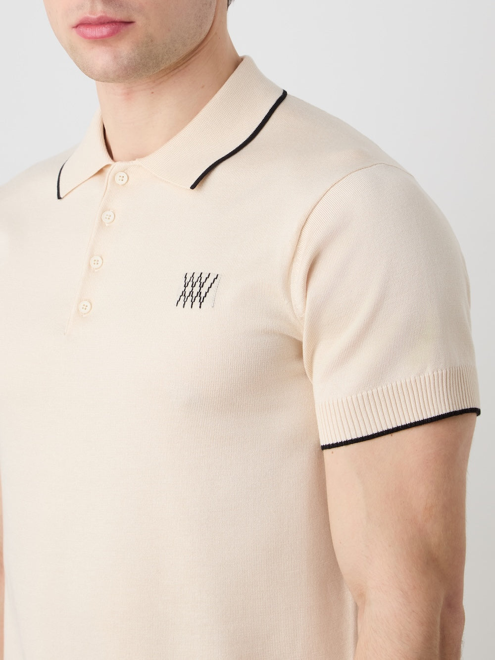 Beige polo shirt with black trim worn by a person on a light background