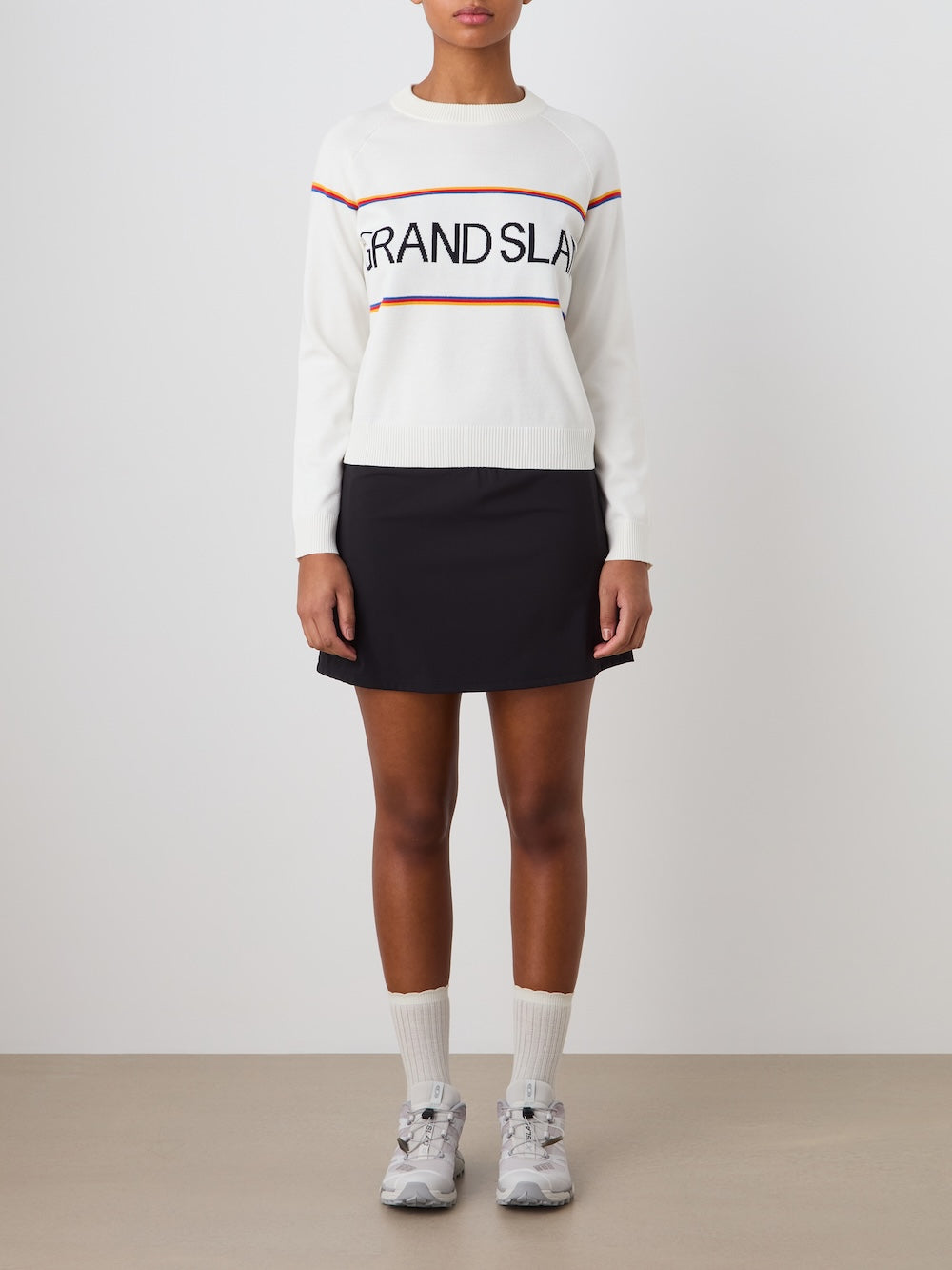 Person wearing a white 'Grand Slam' sweater with a black skirt on a plain background