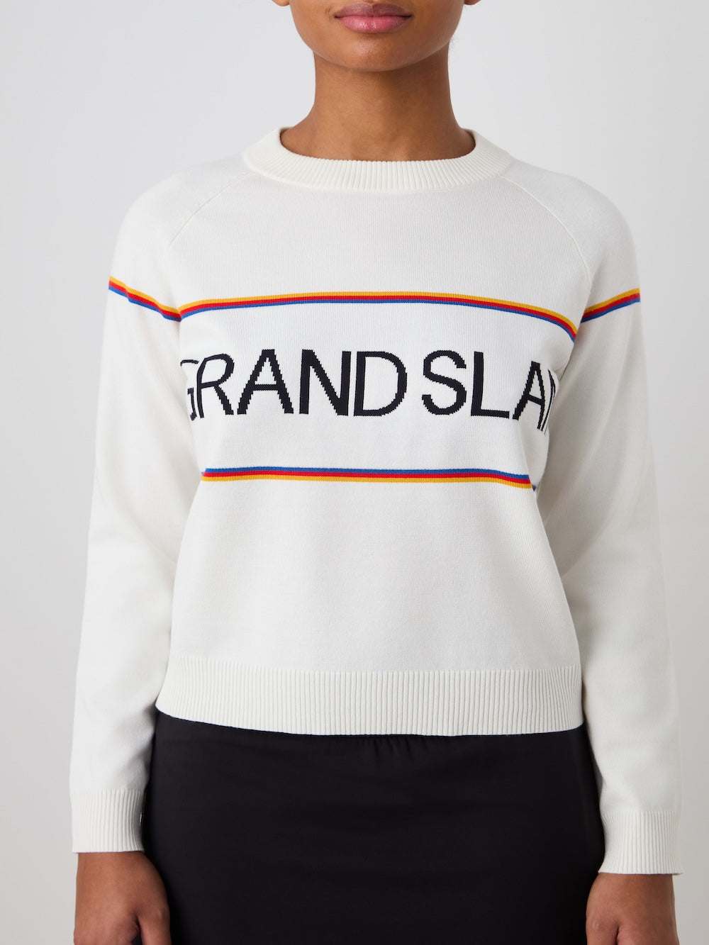 White sweater with 'Grand Slam' text and colorful stripes worn by a person on a light background