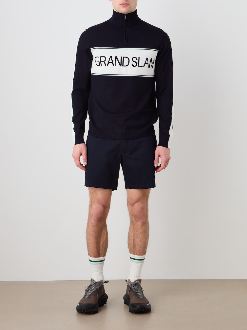Person wearing a navy blue sweater with 'Grand Slam' logo in the front teamed with navy blue shorts on a plain background