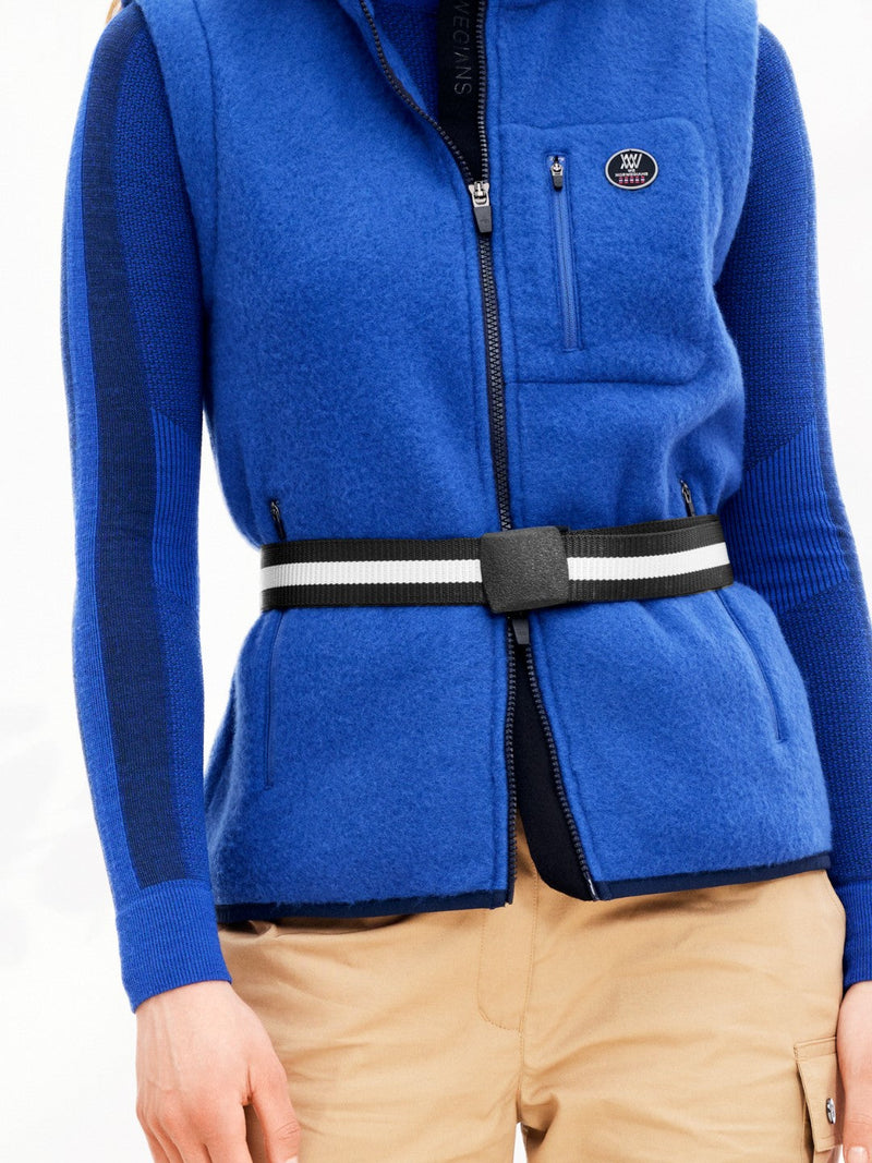 A person is wearing a blue fleece jacket layered over a blue knit sweater and tan pants. The jacket, made of durable polyester, is fastened with the Vidda Belt by We Norwegians, an adjustable black and white belt around the waist. The image emphasizes the upper body and midsection, with no face visible.